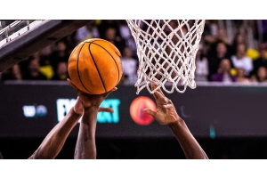 A close-up of the basket, net, and a basketball during a game. Multiple hands reach up for the ball coming off the rim.