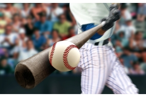 A baseball player is swinging a wooden bat and striking a baseball. A filled stadium is in the background.
