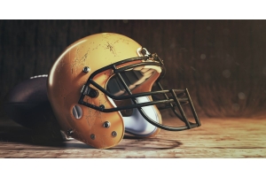 A close-up of a yellow classic American football helmet with scratches on a wooden table in front of a football.