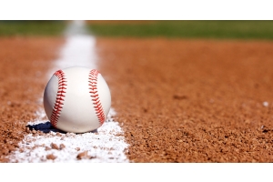 A close-up of a brand new baseball resting on the white chalk foul line in the infield of a baseball diamond.