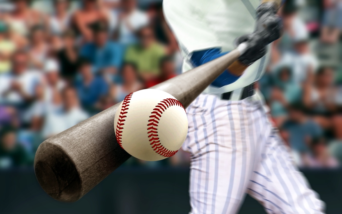 A baseball player is swinging a wooden bat and striking a baseball. A filled stadium is in the background.