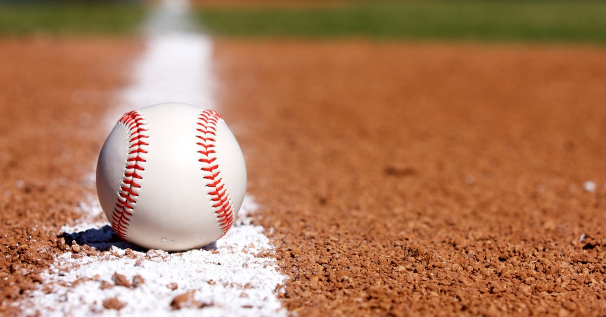 A close-up of a brand new baseball resting on the white chalk foul line in the infield of a baseball diamond.