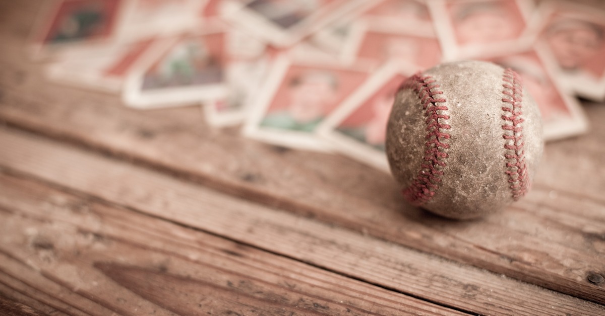 A dirty and used baseball in focus rests on a dirty wooden table with various old baseball cards blurred behind it.