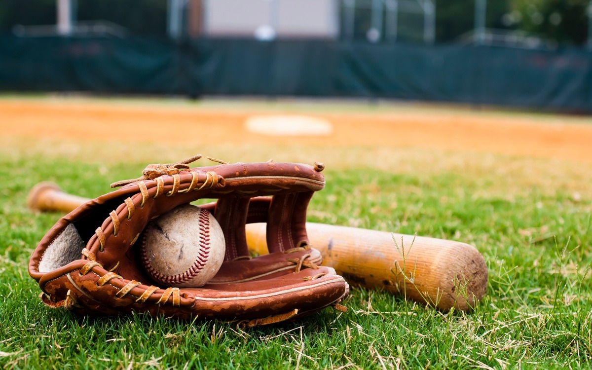 A baseball glove with a baseball in the web. They sit on the infield grass next to a wooden baseball bat.